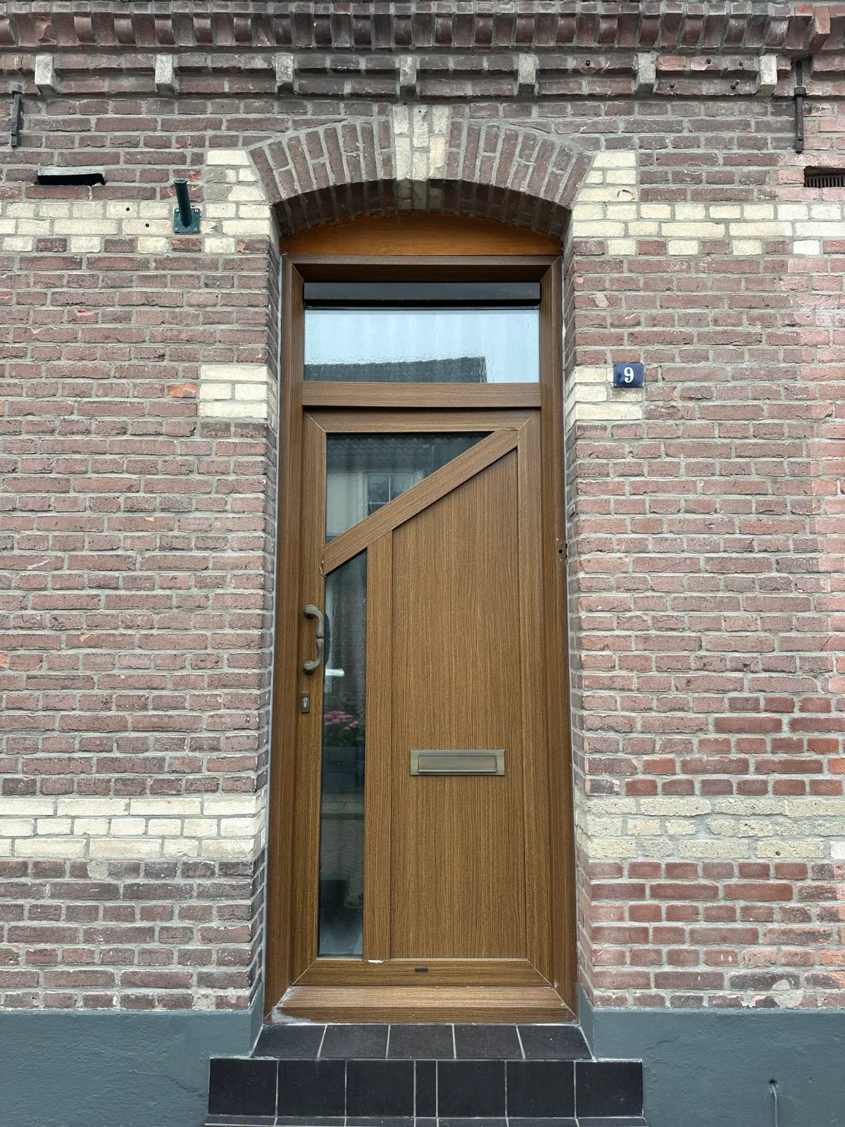 Voor-situatie: oude houten voordeur met sleetse afwerking in baksteengevel